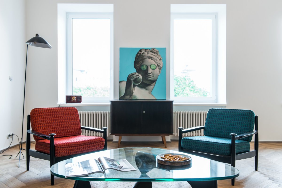 Poster above Blue Settee in White Apartment Interior with Armchair, Wooden Table and Plants. Real photo